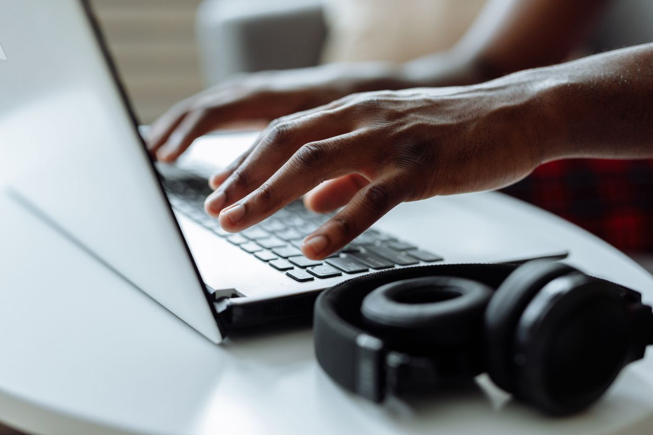 Contact A person typing on a laptop with headphones on a table, ideal for remote work concepts.
